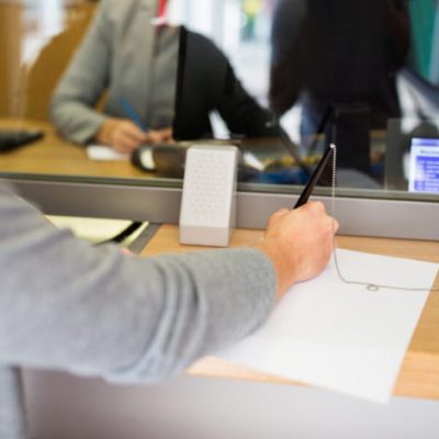 people and finance concept - customer with pen and paper writing application at bank office